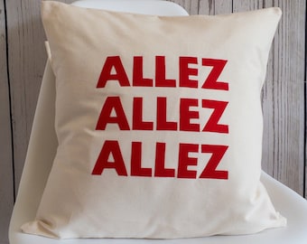 Può includere: Un cuscino bianco con le parole "Allez Allez Allez" stampate in rosso.