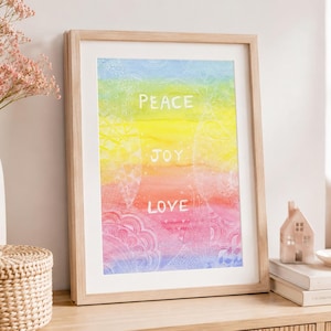 May include: A framed vertical art print featuring a rainbow-colored watercolor background with white hand-lettered text that reads PEACE, JOY, and LOVE. The artwork includes intricate white line-drawn mandala patterns layered over the colors.