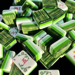 May include: A collection of rectangular mahjong tiles featuring a green bamboo-patterned back and a white face. Some tiles display red Chinese characters, numbers, and floral motifs, while others show a layered green and white side profile.