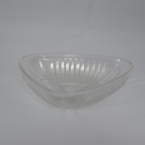 May include: A clear, triangular glass bowl featuring a series of vertical, raised ridges along its interior walls. The bowl has a smooth, rounded rim and a flat base, with the glass material appearing transparent and reflective under the light.