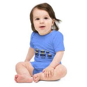 Könnte beinhalten: Ein hellblaues Baby-Body mit dem Text "DAD KING", "MOM QUEEN" und "MINI PRINCE" in Gold und Schwarz. Der Body hat kurze Ärmel und einen runden Ausschnitt. Das Baby sitzt.