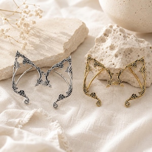 May include: Two ear cuffs shaped like pointed elf ears, one in a silver tone and one in a gold tone. Each cuff features an intricate design of climbing vines, leaves, and small rose blossoms that follow the curve of the ear structure.