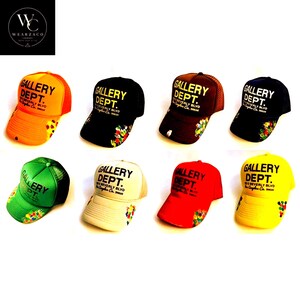 May include: A collection of eight trucker hats in various colors, including orange, black, brown, navy, green, cream, red, and yellow. Each hat features the text "GALLERY DEPT." and a floral design.