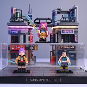 May include: Aura Minifigures display featuring three Lego-style figures with swords, set against a futuristic cityscape with neon signs. The figures have unique hairstyles and outfits. The display case has the text "AURA MINIFIGURES".
