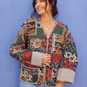 Könnte beinhalten: Eine gesteppte Jacke mit Patchwork-Design, bestehend aus verschiedenen floralen und geometrischen Mustern in Rot-, Grün-, Gelb- und Blautönen. Die Jacke hat einen V-Ausschnitt, lange Ärmel mit braun-weiß gestreiften Bündchen und zwei Vordertaschen.