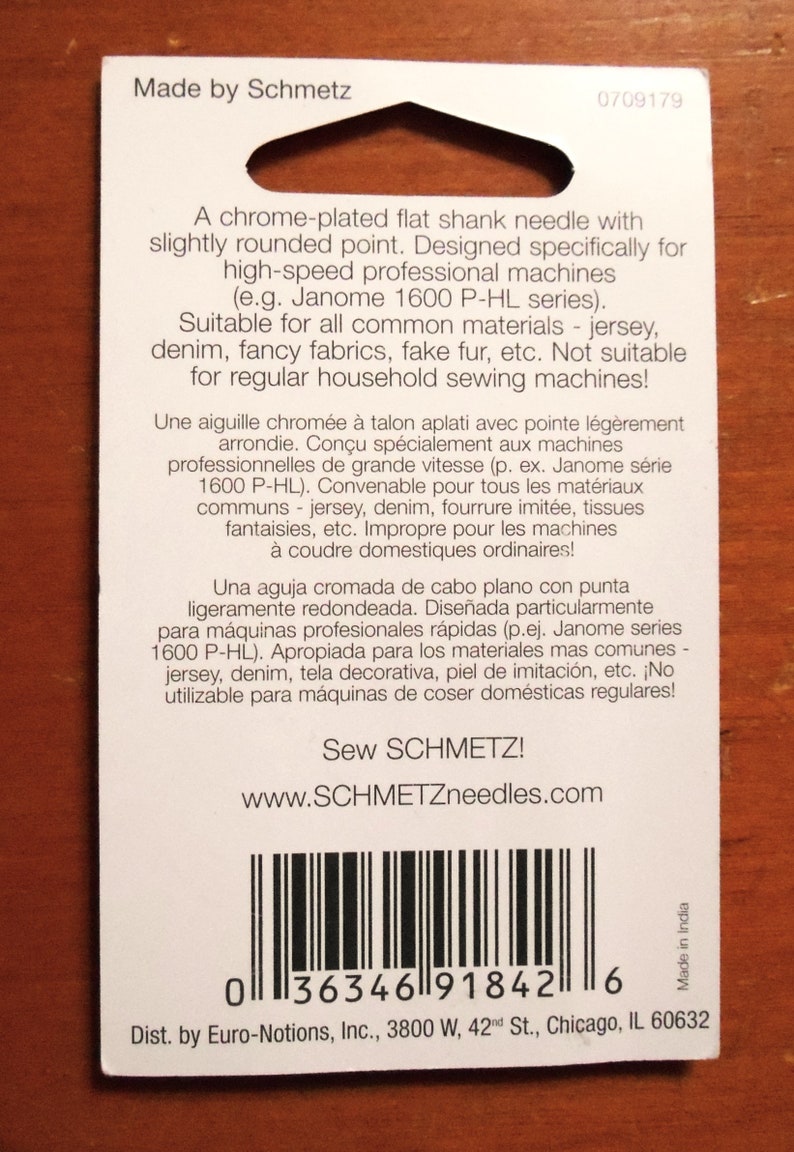 Op de afbeelding: Een witte kaart met tekst en een barcode. De kaart leest "Made by Schmetz" en beschrijft een verchroomde naald met platte schacht voor professionele hogesnelheidsnaaimachines. De tekst bevat ook de website www.SCHMETZneedles.com.