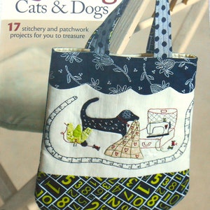 May include: A fabric tote bag with the title "It's Quilting Cats & Dogs" and illustrations of a dog, bird, and sewing machine. The bag has a navy blue floral top, polka dot handles, and a number pattern at the bottom.