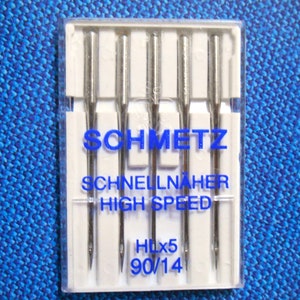 Op de afbeelding: Een verpakking Schmetz-naaimachinenaalden. De naalden zijn zilverkleurig en zitten in een doorzichtige plastic verpakking. De tekst op de verpakking luidt "SCHMETZ SCHNELLN&Auml;HER HIGH SPEED HLx5 90/14". De achtergrond is een blauwe stof.