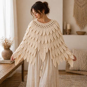 Puede incluir: Capa de ganchillo hecha a mano de color crema, con un diseño en forma de plumas. La capa presenta un escote redondo y elementos en forma de hojas. La prenda forma parte de un atuendo de estilo bohemio, combinada con una falda larga y fluida.