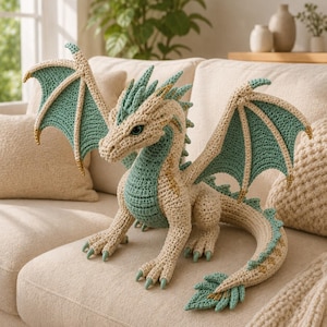 May include: A crocheted dragon plush toy featuring a cream-colored body with teal accents on the wings, spine, and tail. The creature has a detailed head with prominent ridges, large eyes, and a long, curved tail with a leaf-shaped tip.