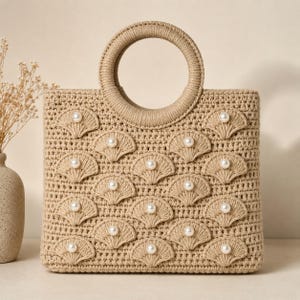 Puede incluir: Un bolso de ganchillo beige con cuerpo cuadrado y asa circular. La superficie frontal está decorada con un patrón repetitivo de motivos de ganchillo en forma de abanico, cada uno con una cuenta de perla blanca en el centro.