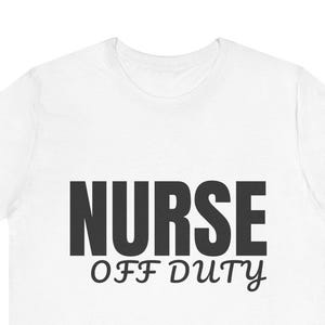 May include: White t-shirt with the words "NURSE OFF DUTY" printed in black. The word "NURSE" is in a bold, block font, while "OFF DUTY" is in a script font. The shirt is made of a soft material.
