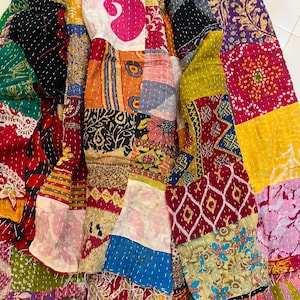 Puede incluir: Un textil de patchwork que presenta una variedad de cuadrados de tela coloridos cosidos con hilo blanco visible. La tela muestra diversos patrones, incluyendo estampados florales, geométricos y de cachemira en tonos rojos, amarillos, azules, verdes y rosas.