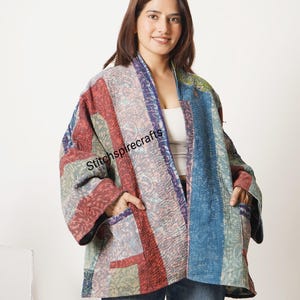 Könnte beinhalten: Eine gesteppte Jacke im Kimono-Stil mit einem Patchwork-Design aus vertikalen Streifen in Rot-, Blau- und Grüntönen. Das Kleidungsstück hat weite Ärmel, zwei Vordertaschen und den Text Stitchspirecrafts auf dem Vorderteil aufgedruckt.