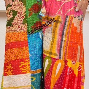 May include: Wide-leg pants featuring a vibrant patchwork design with various floral and geometric patterns in red, orange, green, blue, and yellow. The pants have an elastic waistband with a drawstring and visible white kantha stitching.