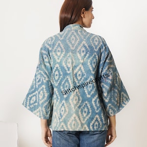 May include: A blue and white patterned kimono-style jacket featuring a repeating diamond motif and wide sleeves. The fabric displays a textured appearance with a faded indigo dye effect. The text Stitchspirecrafts is printed across the back.