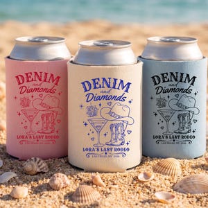 Op de afbeelding: Drie blikjeskoelers in roze, beige en blauw, elk met een "Denim and Diamonds"-ontwerp. Het ontwerp omvat een cowboyhoed, laarzen, een martiniglas en de tekst "Lora's Last Rodeo, Las Vegas, NV 2026."