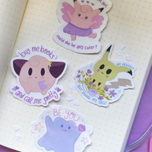 Könnte beinhalten: Eine Sammlung farbenfroher Aufkleber mit Cartoon-Charakteren und Texten. Ein Aufkleber zeigt einen rosa Charakter mit dem Text "who's that wonderful girl, could she be any cuter?". Ein anderer sagt "buy me books and call me pretty".