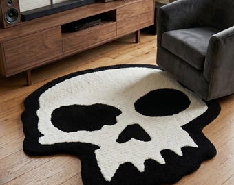Könnte beinhalten: Ein großer, geformter Teppich mit einem kontrastreichen Design eines menschlichen Schädels. Der Teppich ist überwiegend weiß mit einem dicken schwarzen Rand sowie schwarzen Augenhöhlen und Nasenöffnung. Er hat eine texturierte, getuftete Oberfläche.