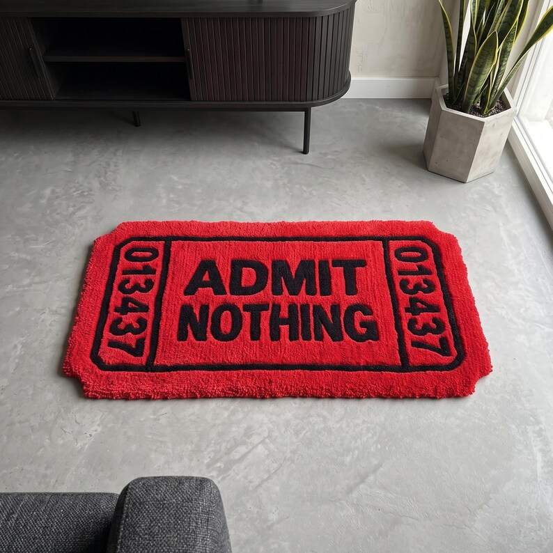 Puede incluir: Una alfombra rectangular roja de pelo insertado con forma de entrada de cine antigua. La alfombra presenta un borde negro y el texto "ADMIT NOTHING" en letras negras en negrita en el centro, con el n&uacute;mero "013437" impreso a ambos lados.