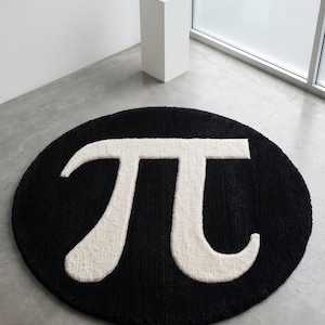 Könnte beinhalten: Ein runder Teppich mit schwarzem Hintergrund und einem großen, mittig platzierten weißen mathematischen Pi-Symbol. Der Teppich hat eine dicke, getuftete Textur und liegt flach auf einem glatten, hellgrauen Boden in einem hellen Raum.
