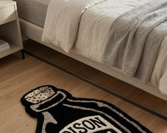 Puede incluir: Una alfombra de mechones en blanco y negro con forma de botella y tapón de corcho. La alfombra presenta la palabra POISON en letras negritas sobre un gráfico de calavera y tibias cruzadas. El diseño está delineado en gris y negro.