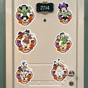 May include: Six circular Halloween-themed wall decals featuring Disney characters including Mickey Mouse as Frankenstein, Minnie Mouse, Donald Duck, Daisy Duck, Goofy, and Pluto in mummy attire. Each decal includes a wreath border and a name placeholder.