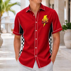 May include: A short-sleeve button-down shirt in bright red with white piping along the collar and front placket. The shirt features a yellow lightning bolt graphic with the number 95 in red and black, and black and white checkered side panels.