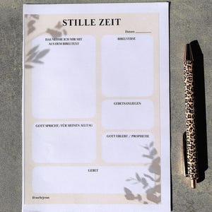 Könnte beinhalten: Ein rechteckiges Planerblatt mit der Überschrift STILLE ZEIT, unterteilt in Bereiche für Notizen, Bibelverse, Gebetsanliegen und tägliche Reflexionen, auf beigem Hintergrund mit Blatt-Schattenwurf, neben einem Kugelschreiber mit Leopardenmuster.