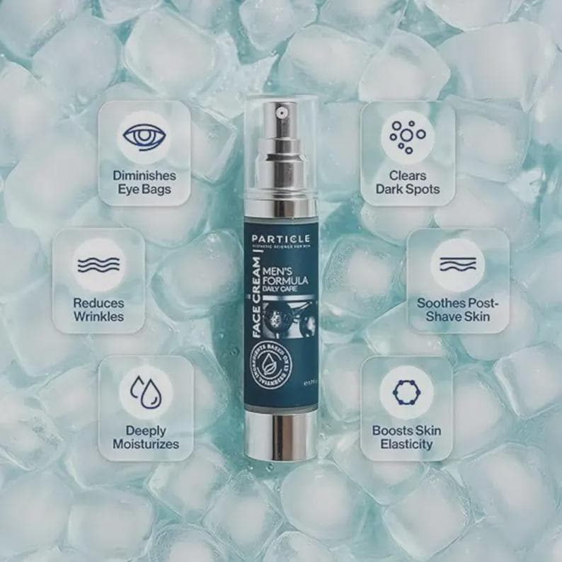 Op de afbeelding: Een zilveren en marineblauwe Particle Men's Formula Face Cream fles met een sproeikop, omringd door ijsblokjes. Het product beweert wallen te verminderen, rimpels te verminderen, diep te hydrateren, donkere vlekken te verwijderen, de huid na het scheren te verzachten en de huidelasticiteit te stimuleren.