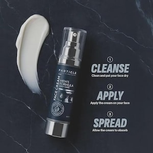 Op de afbeelding: Een huidverzorgingsproductfles met een pompdosser, met het label "Particle Men's Formula Daily Care Face Cream". Een witte cr&egrave;meveeg ligt naast de fles. Instructies: Reinigen, Aanbrengen, Verspreiden.