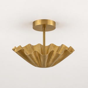 May include: A brass ceiling light fixture featuring a central vertical rod attached to a circular canopy. The light has a wide, bowl-shaped shade with a distinctively wavy, scalloped edge, finished in a brushed metallic gold tone throughout.