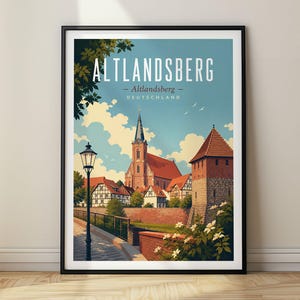 May include: A framed travel poster featuring a stylized illustration of Altlandsberg, Germany. The print displays a church with a tall steeple, a stone tower, half-timbered houses, a street lamp, and white flowers under a blue sky with clouds.