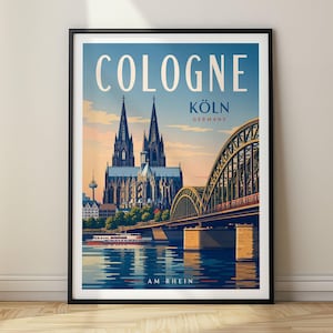 May include: A framed travel poster featuring the Cologne Cathedral and the Hohenzollern Bridge over the Rhine River. The text reads COLOGNE, KÖLN, GERMANY, and AM RHEIN. The illustration uses a palette of blue, orange, and green tones.