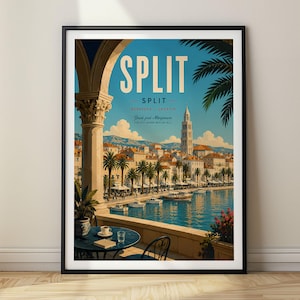 May include: A framed travel poster featuring a view of Split, Croatia, from a balcony with a stone archway. The scene shows a harbor with boats, palm trees, a bell tower, and a blue sky. A small table with a cup and book sits in the foreground.