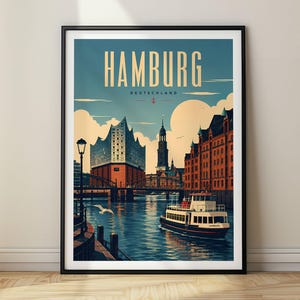 May include: A framed travel poster of Hamburg, Germany, featuring the Elbphilharmonie, a church spire, and red brick buildings along a canal. A passenger boat travels on the water under a blue sky with clouds. The text reads HAMBURG DEUTSCHLAND.