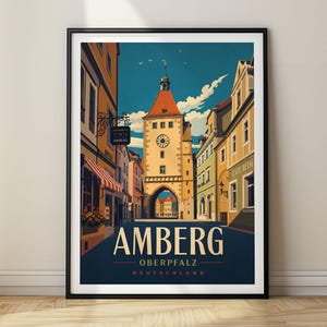 Könnte beinhalten: Ein gerahmtes Reiseplakat mit einer Straßenszene in Amberg, Deutschland. Die Illustration zeigt einen zentralen Uhrturm mit rotem Dach, flankiert von farbenfrohen Gebäuden, einem blauen Himmel mit Wolken und dem Text AMBERG OBERPFALZ DEUTSCHLAND.
