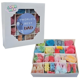 May include: A white square gift box containing assorted sour gummy candies in sixteen individual compartments. The box features a scalloped window, a SOUR MIX label, and a circular blue sticker with the text WORLD'S BEST DAD in copper.