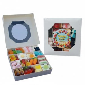 Può includere: Una scatola regalo bianca con una varietà di caramelle gommose colorate. Le caramelle sono disposte a griglia, con forme come fiori, frutta e altri disegni divertenti. La scatola è aperta, rivelando le prelibatezze.