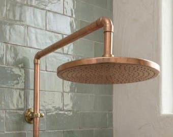 May include: A wall-mounted shower head with a circular, perforated face and a long, horizontal arm. The fixture is constructed from copper-toned metal, featuring a polished finish and a simple, industrial-inspired pipe design.