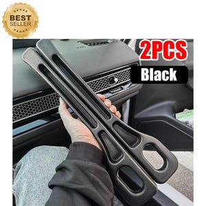May include: Two black car interior door handle covers. The covers have a textured surface and a long, rectangular shape with a curved handle. The text "2PCS Black" is visible in the image, along with a "Best Seller" badge.