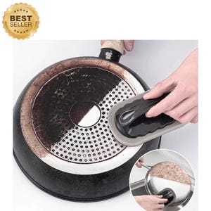 May include: A black and gray cleaning sponge is used to scrub the bottom of a dirty, black frying pan. The pan has a circular perforated area and a handle. A "Best Seller" sticker is in the upper left corner.