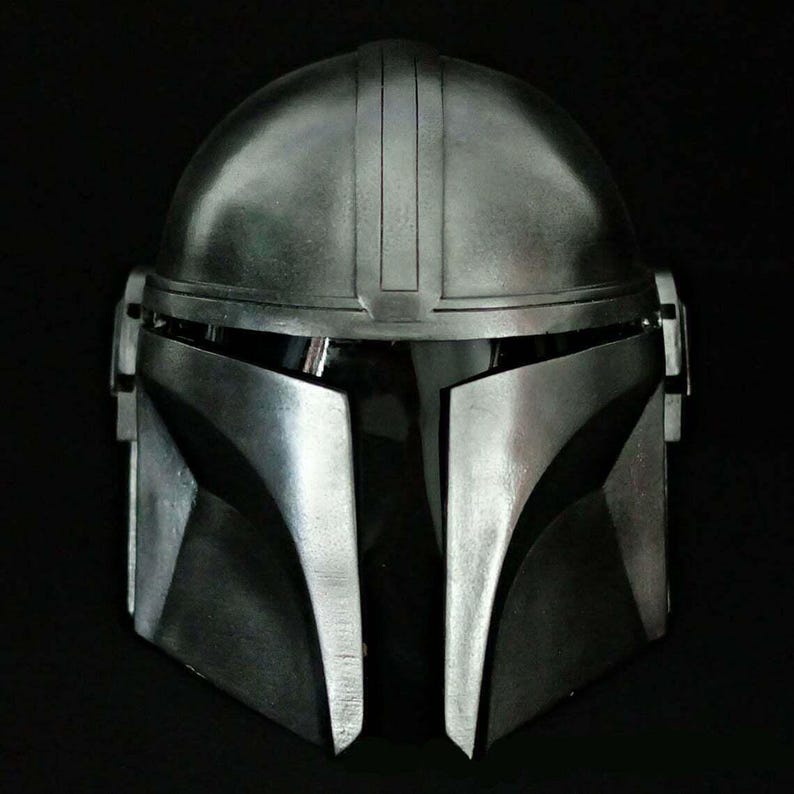 May include: A metallic silver Mandalorian helmet with a dark visor. The helmet has a rounded top with vertical ridges and angular cheek plates. The helmet is designed with a sleek, futuristic aesthetic, perfect for cosplay or display.