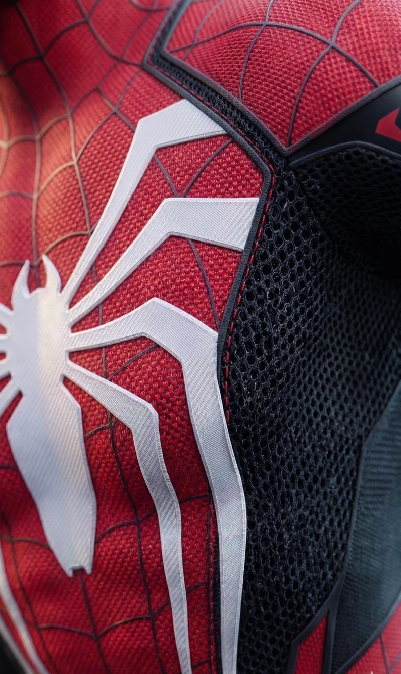 May include: Close-up of a red and black Spider-Man costume. The costume features a white spider emblem on the chest and white web patterns. The suit has a textured fabric and black mesh detailing.