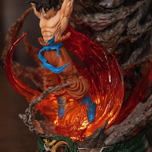 May include: A detailed figurine of a muscular character in a dynamic pose, surrounded by fiery orange and red energy effects. The figure wears orange pants, blue boots and wristbands, and a blue sash. The base features a dragon design.