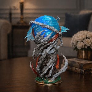 May include: A detailed sculpture featuring a blue orb with swirling patterns, surrounded by gray, cloud-like formations and red accents. The base has a green and gold trim. The artwork is displayed on a dark wooden table.