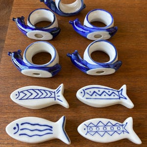 Peut inclure: Ensemble de vaisselle en céramique comprenant des ronds de serviette en forme d'escargot et des pièces de service en forme de poisson. Les ronds de serviette sont blancs avec des détails bleus. Les pièces en forme de poisson sont blanches avec des motifs bleus.