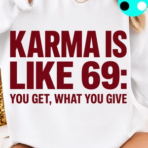 May include: A white crewneck sweatshirt featuring bold, dark red text that reads: KARMA IS LIKE 69: YOU GET, WHAT YOU GIVE. The design is centred on the front of the garment, which has long sleeves and a ribbed neckline, presented in a clean, simple style.