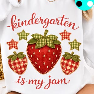 May include: A white sweatshirt featuring a graphic of three strawberries with red and white gingham patterns and green leaves. The text reads kindergarten is my jam in red cursive script. Four small gingham stars in red and green surround the fruit.