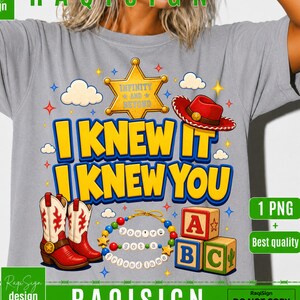 Op de afbeelding: Een grijs t-shirt met een grafische print met de tekst I KNEW IT I KNEW YOU in gele letters. Het ontwerp bevat een gele sheriffster, een rode cowboyhoed, rood-witte cowboylaarzen, een kralenketting en drie blokken met letters erop.